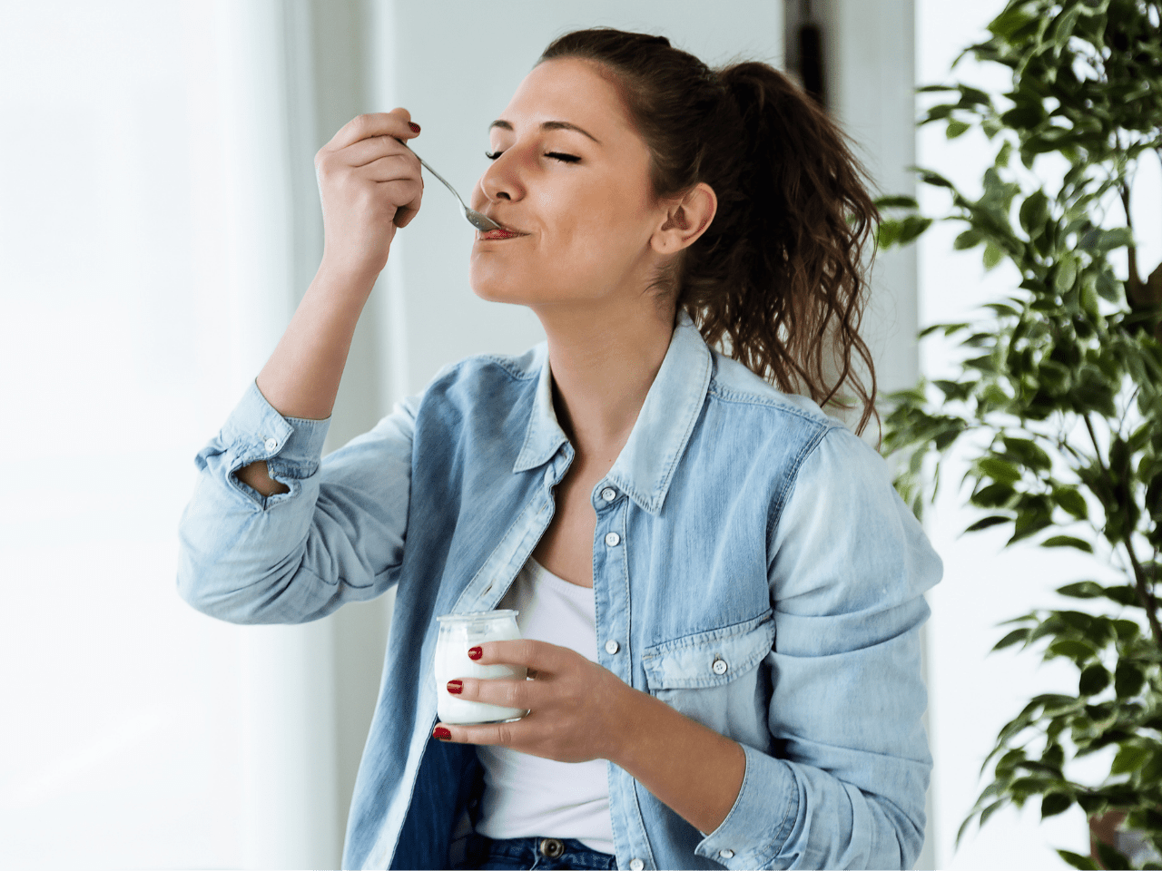 Mujer comiendo yogurt con los ojos cerrados, disfrutando con calma y presencia, simbolizando una relación más tranquila con la comida.