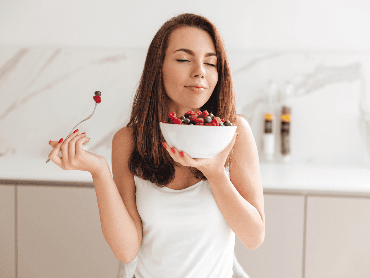 Mujer con un bowl de fresas oliéndolo con expresión relajada, representando comer con más paz y reducir el comer emocional sin culpa.