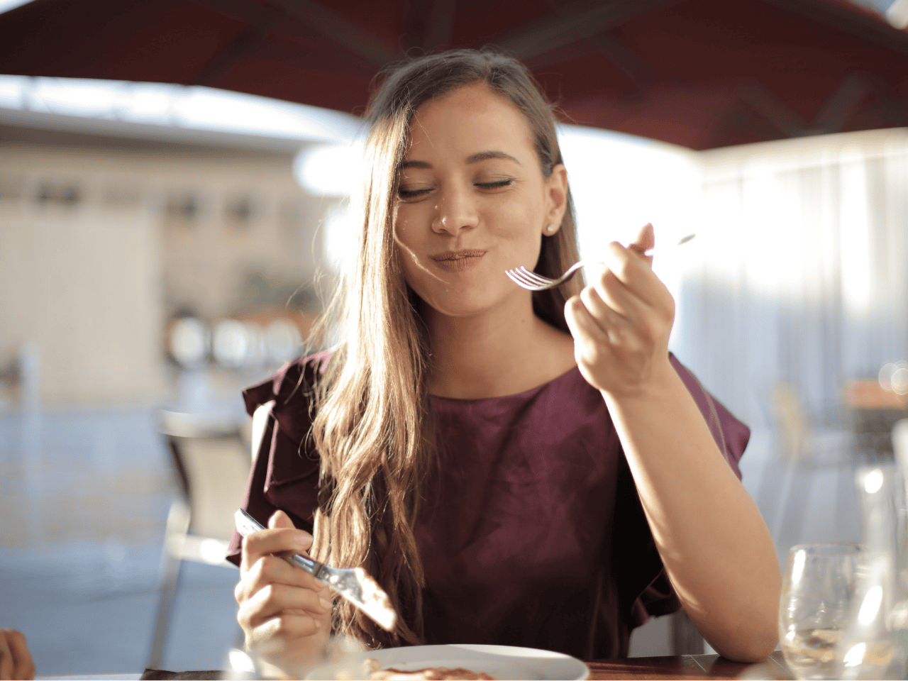 Mujer comiendo con expresión relajada, representando paz al comer y hábitos sostenibles sin culpa en Transforma tu relación con la comida.