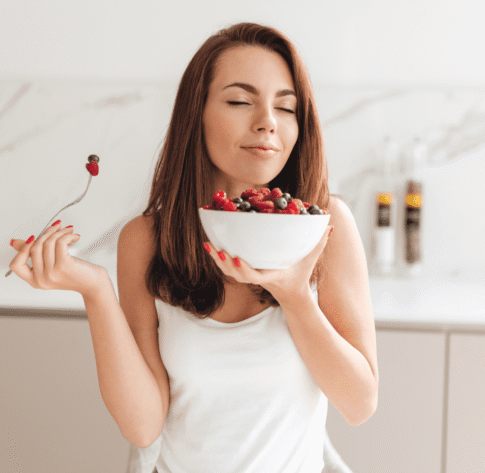 Mujer tranquila con los ojos cerrados sosteniendo un bowl de frutos rojos, representando bienestar y calma tras aplicar lo aprendido en el curso Nutriendo tu Bienestar.