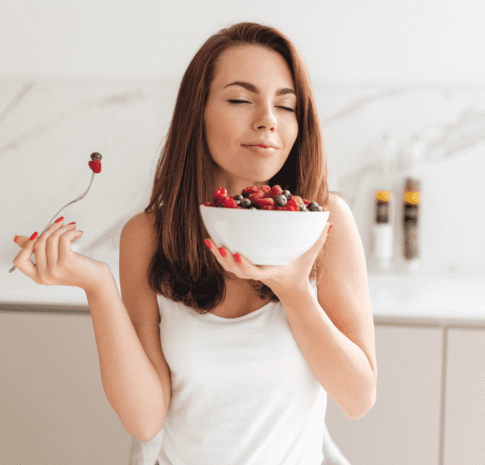 Mujer con los ojos cerrados sosteniendo un bowl de frutos rojos, representando calma, bienestar y confianza después de obtener claridad sobre su alimentación.